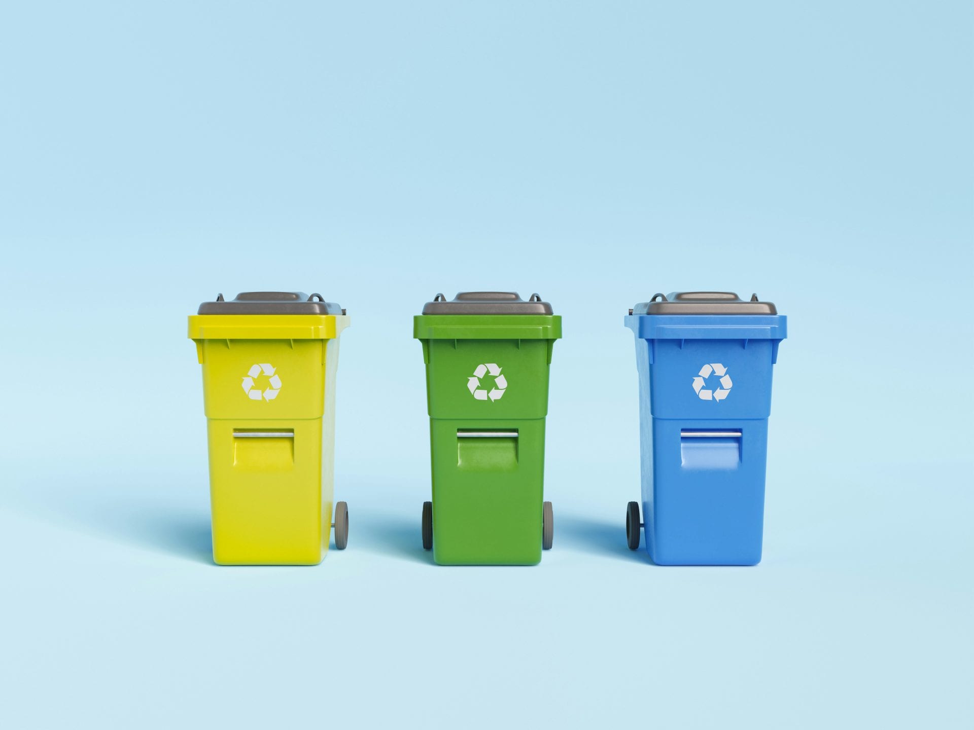 drei recycling tonnen gelb, grün und blau stehen nebeneinander vor einem hellblauen hintergrund. jede tonne hat ein weißes recycling symbol auf der vorderseite und ist mit rädern und einem geschlossenen deckel ausgestattet.